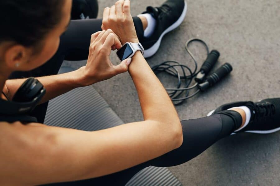 Woman fiddling with smart watch wearable and skipping rope in background