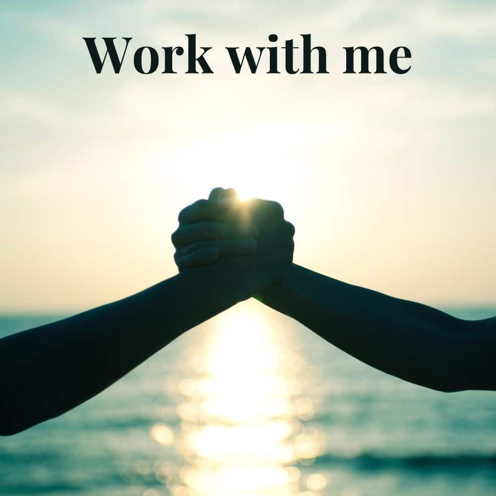 Two people's hands grabbing each other in support silhouetted against a sunrise over the ocean