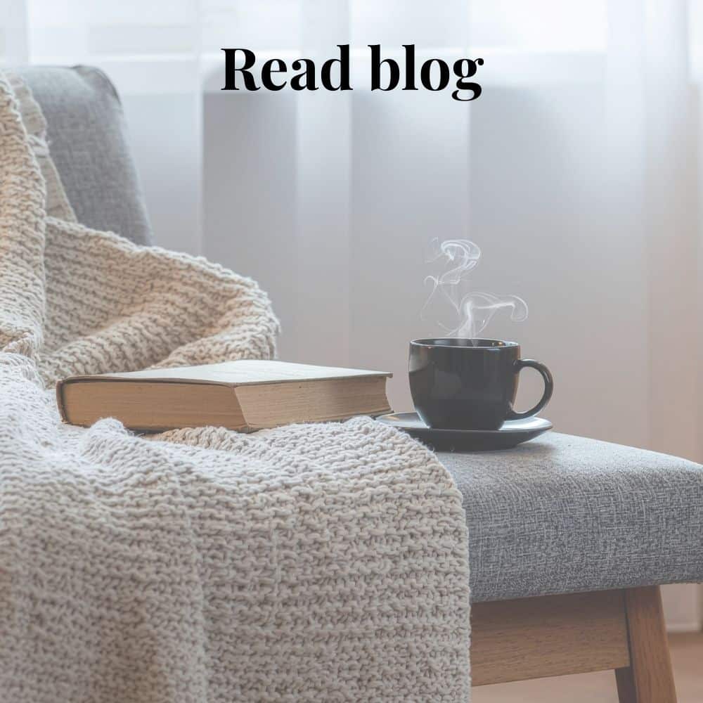 Steaming cup of hot drink next to a book lying on a throw on a chair